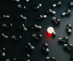 One lit lightbulb surrounded by black lightbulbs