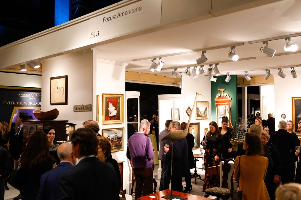 People at an art fair with paintings and antiques.