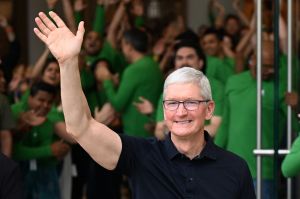 Man in black shirt waves to crowd, people in green shirts stand behind him