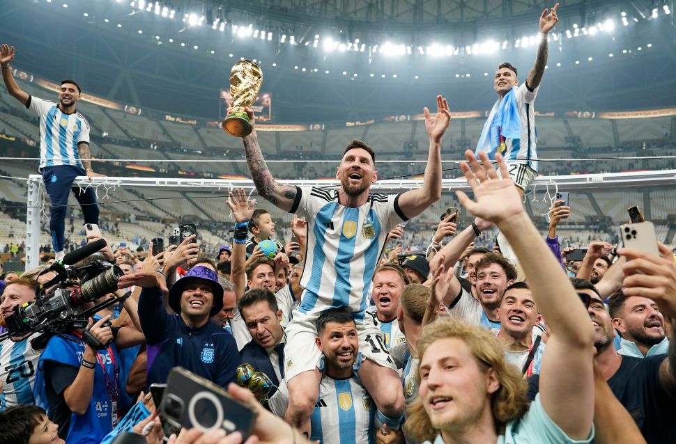 Image of soccer player (Lionel Messi) celebrating on players' shoulders with a golden trophy 