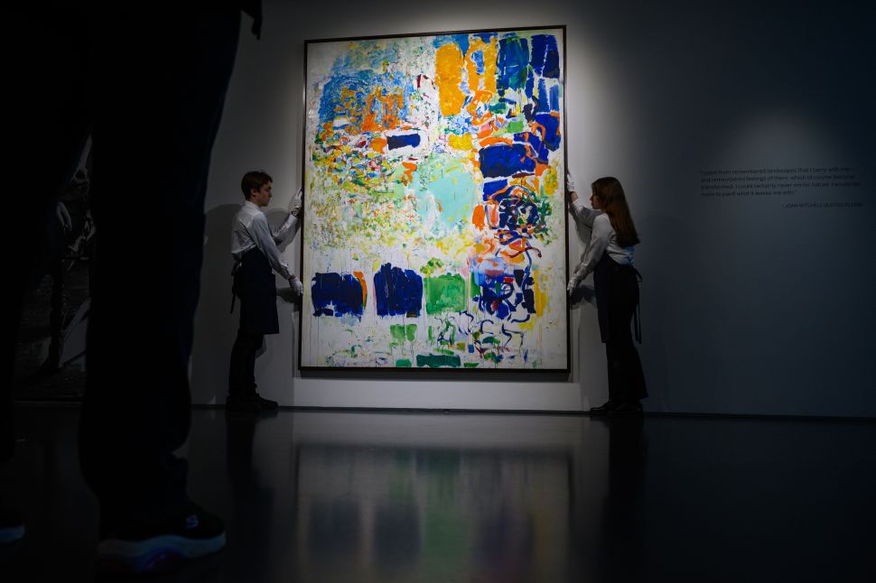 Two art handlers carefully adjust a large abstract painting by Joan Mitchell on the wall, with the reflection of the artwork visible on the polished floor.