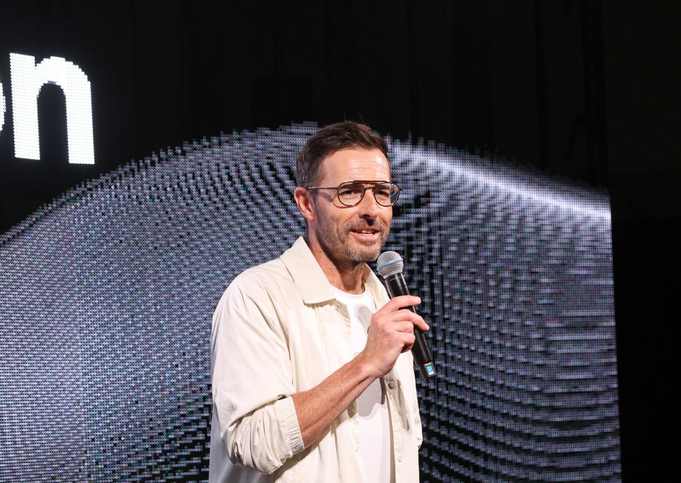 Man in white shirt stands onstage and speaks into microphone