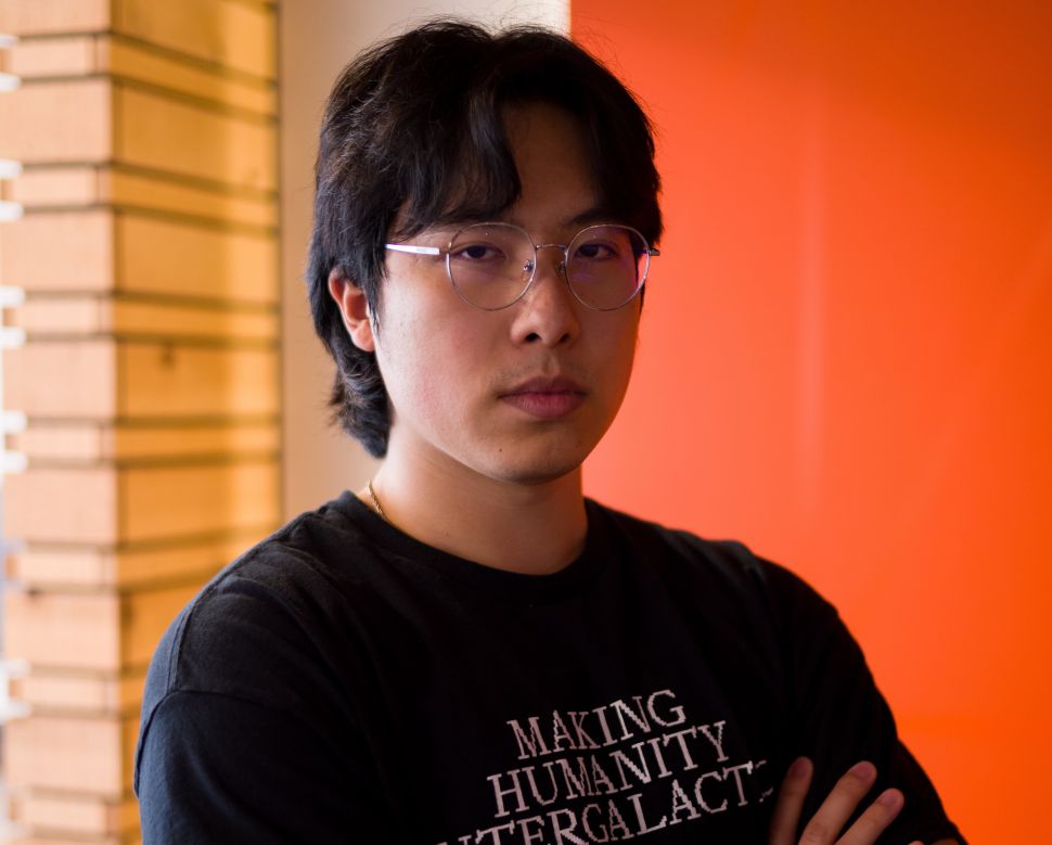 Image of man in glasses and black T-shirt posing in front of orange background